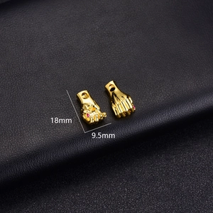 Detail of 14K gold plated hand charms with red zircon inlay on black leather background