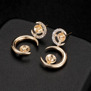 Golden moon-shaped earrings with zircon accents and pearl mounts on a black texture