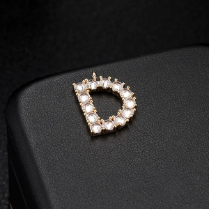Detalle macro del colgante letra D dorada con engaste de circonitas micro-pavé brillantes