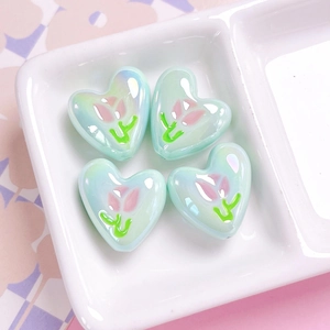 Macro shot of mint green heart-shaped resin beads with tulip patterns and iridescent finish