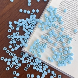 Macro shot of light blue acrylic square beads with large holes on a wooden background