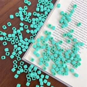 Macro view of mint green square acrylic beads with center holes on a wooden desk