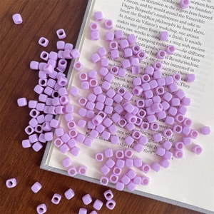 Macro detail of square purple acrylic beads with central hole on a vintage book page