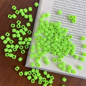 Macro shot of fluorescent green acrylic square beads with holes on a dark wooden table