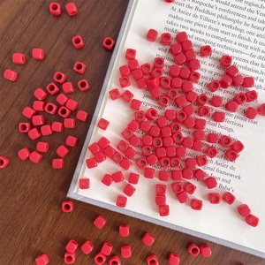 Close-up of red acrylic square beads with large holes on vintage book pages for DIY craft