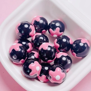 Macro shot of glossy black round beads with hand-painted pink flower patterns for DIY jewelry