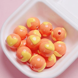 Close-up of bright orange DIY beads with yellow heart patterns in a white tray