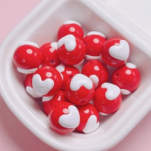 Macro shot of red acrylic round beads featuring white embossed heart shapes for DIY jewelry