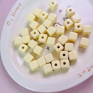 Close-up of 12mm macaron yellow acrylic square beads with center holes on a ceramic plate