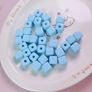 Macro shot of 12mm light blue acrylic cube beads in a white ceramic decorative plate