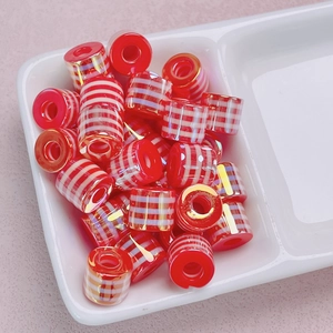 Macro view of red cylindrical striped barrel beads with gold metallic grid for DIY jewelry