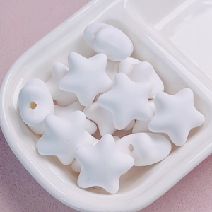 Macro view of macaron white star beads and round acrylic charms in a ceramic tray