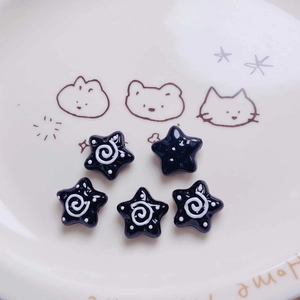 Macro shot of five black star-shaped acrylic beads with white swirl and polka dot patterns