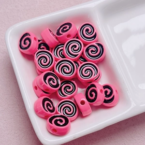 Macro shot of pink and black spiral acrylic beads for DIY jewelry making in a ceramic tray