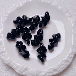 Macro shot of 9 black spiral acrylic beads on a white vintage porcelain tray for DIY crafts
