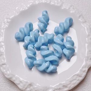 Macro detail of light blue acrylic spiral beads for DIY jewelry in a white ceramic dish