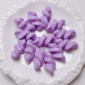 Top view of lavender acrylic twisted spiral beads arranged on a white floral ceramic plate