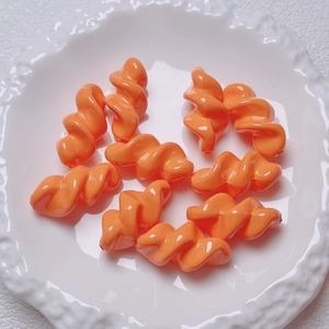 Polished orange acrylic spiral beads for DIY jewelry displayed on a white ceramic tray