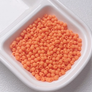 Macro view of 4mm matte orange beads in a white container for DIY jewelry making