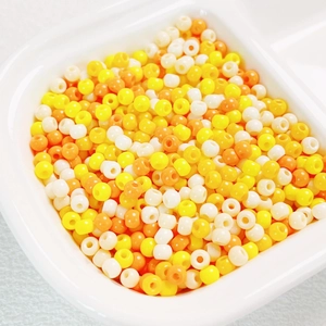 Close-up of 4mm high-quality lemon yellow, orange and white glass seed beads in a tray