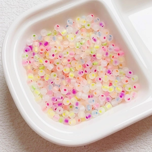 Macro shot of 4mm matte translucent glass seed beads with colorful dots in a white tray
