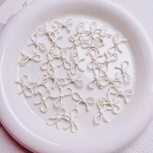 Detailed view of matte white bow-shaped alloy beads on a ceramic plate for DIY jewelry