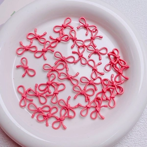Close-up of cute pink bow-shaped alloy beads for DIY jewelry making in a white tray