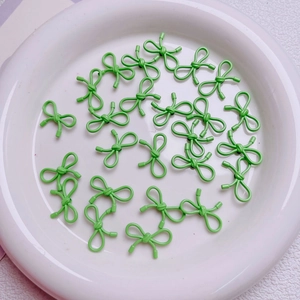 Macro detail of light green metal bow charms for DIY jewelry making on white ceramic plate