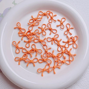 Close-up of bright orange alloy bow beads for DIY jewelry and phone chain accessories