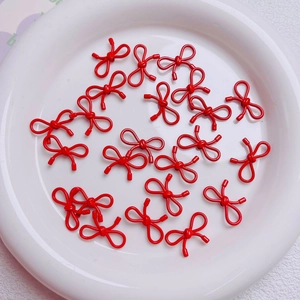 Close-up of small red bow-shaped alloy charms for DIY jewelry making in a white ceramic dish