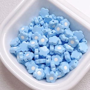 Macro detail of blue acrylic flower beads for DIY jewelry making in a white ceramic bowl