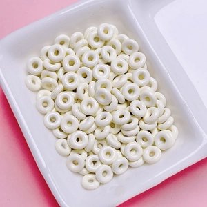 Close-up of white donut-shaped alloy beads for DIY jewelry making in a ceramic tray