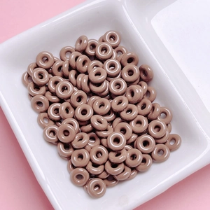 Macro shot of glossy chocolate brown donut-shaped beads in a white sorting tray