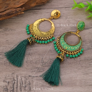 Detalle de pendientes bohemios dorados con cuentas verdes y borlas de 11 cm