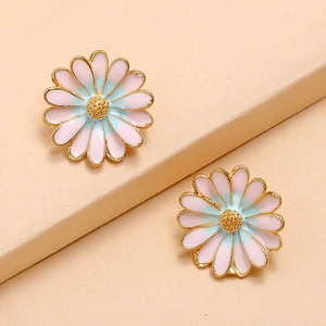 Detail of pink and blue enamel daisy earrings with gold trim on a beige stand