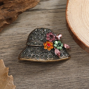Vintage bronze hat brooch with grey crystals and colorful rhinestones on wood background