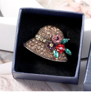 Detailed view of bronze straw hat brooch with amber rhinestones in a blue jewelry box