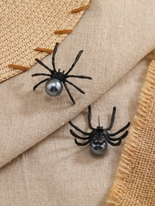 Vista detallada de pendientes de araña negros con perla gris sobre fondo de lino natural