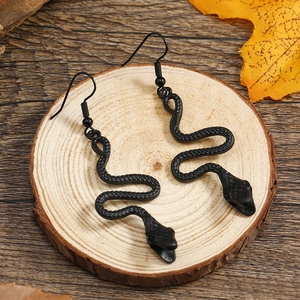 Detail of gothic black snake earrings featuring a textured serpent design on wood