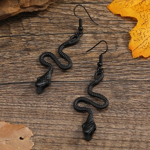 Detail view of matte black snake earrings with scales on dark wood and autumn leaves