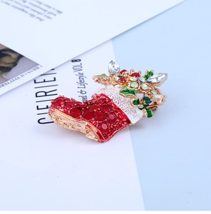 Détail d'une broche chaussette de Noël dorée avec émail rouge et strass brillants