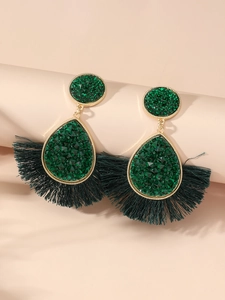 Close-up of bohemian fan-shaped fringe earrings with dark green crystal and gold metal
