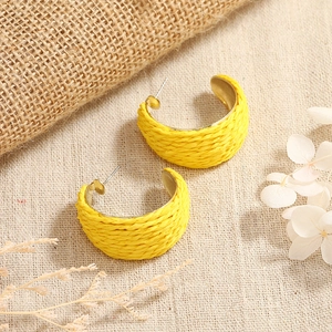 Detail view of bright yellow woven C-shaped earrings with gold metal base on beige fabric