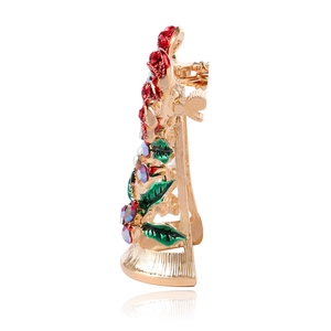 Side view of golden Christmas bell brooch with red rhinestones and green leaves detail