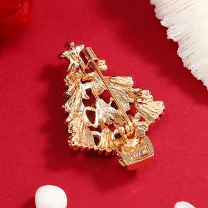 Creative gold Christmas tree brooch with colorful gems on festive red background