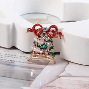 Macro shot of Christmas bell brooch with red rhinestone bow and green enamel leaves