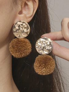 Detail van gouden oorbellen met gehamerde metalen schijf en bruine fluwelen pompon