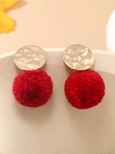 Detail van rode fluwelen pompon oorbellen met gehamerd gouden metalen studs op display