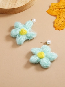 Detail of blue knitted flower earrings with a white pearl and soft yarn texture