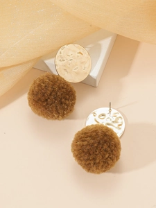 Detail van fluwelen pompon oorbellen met gehamerde gouden schijven op beige basis